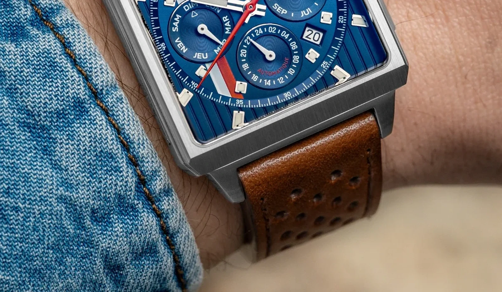 Partie inférieure d’une montre rectangulaire à cadran bleu portée avec un bracelet en cuir marron perforé